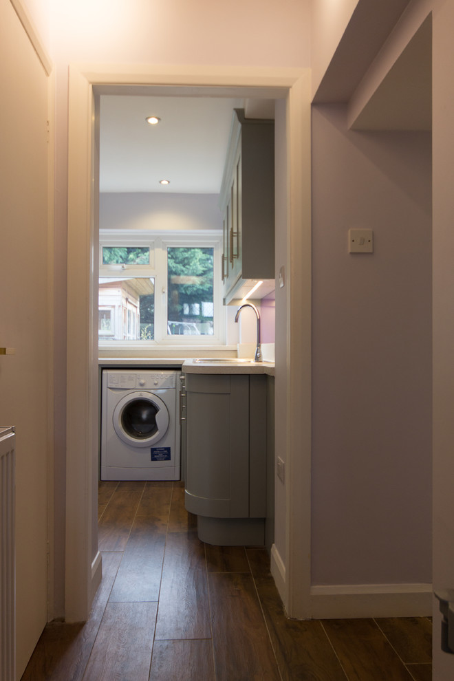 Photo of a mid-sized modern l-shaped dedicated laundry room in London with a single-bowl sink, shaker cabinets, grey cabinets, laminate benchtops, purple walls, porcelain floors and a side-by-side washer and dryer.