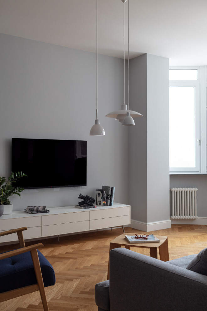 На фото: объединенная, серо-белая гостиная комната среднего размера в скандинавском стиле с серыми стенами, паркетным полом среднего тона, телевизором на стене, зоной отдыха и коричневым полом без камина