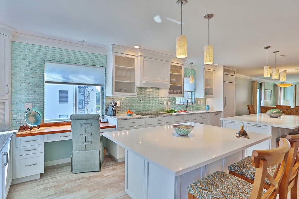 Inspiration for a large beach style galley eat-in kitchen in Tampa with an undermount sink, white cabinets, granite benchtops, blue splashback, glass tile splashback, stainless steel appliances, light hardwood floors, multiple islands and recessed-panel cabinets.