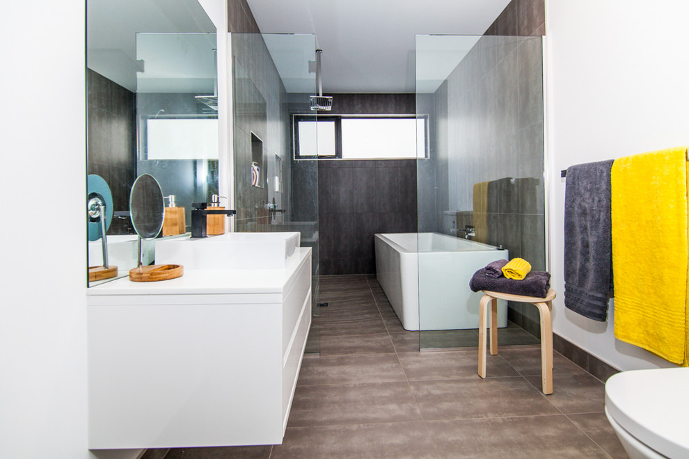 Photo of a small contemporary bathroom in Hobart with flat-panel cabinets, white cabinets, a freestanding tub, an open shower, a one-piece toilet, gray tile, ceramic tile, white walls, ceramic floors, a vessel sink and laminate benchtops.