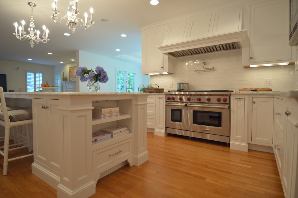 Inspiration for a transitional u-shaped medium tone wood floor eat-in kitchen remodel in Boston with a farmhouse sink, beaded inset cabinets, white cabinets, marble countertops, white backsplash, subway tile backsplash, stainless steel appliances and an island