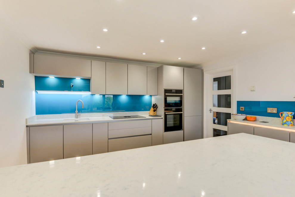 Design ideas for a medium sized modern grey and white single-wall kitchen/diner in Sussex with a submerged sink, flat-panel cabinets, grey cabinets, quartz worktops, blue splashback, glass sheet splashback, integrated appliances, vinyl flooring, an island, brown floors, white worktops and feature lighting.