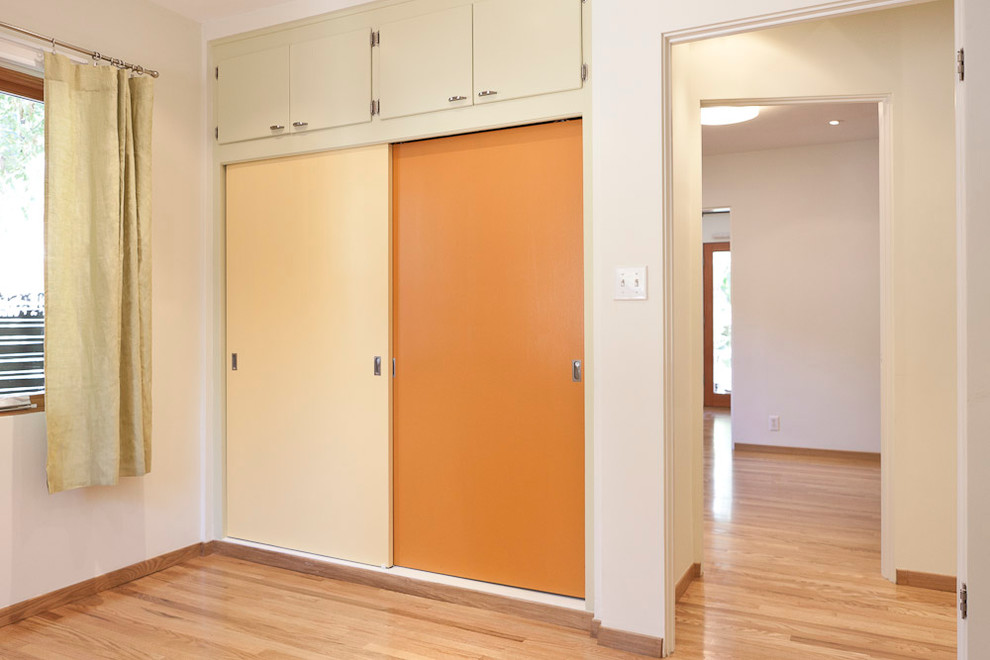 Photo of a small modern gender-neutral built-in wardrobe in Portland with flat-panel cabinets, orange cabinets and light hardwood floors.