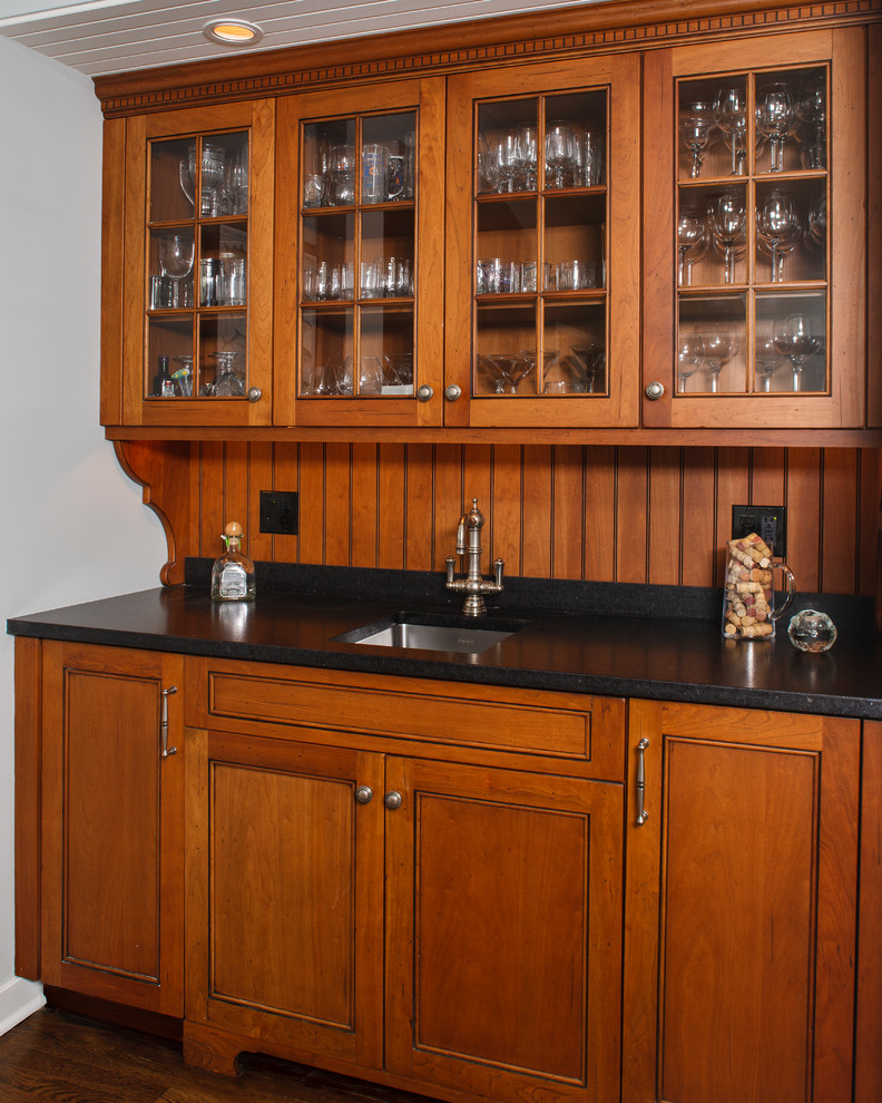 Photo of a transitional single-wall wet bar in New York with an undermount sink, recessed-panel cabinets, medium wood cabinets and soapstone benchtops.