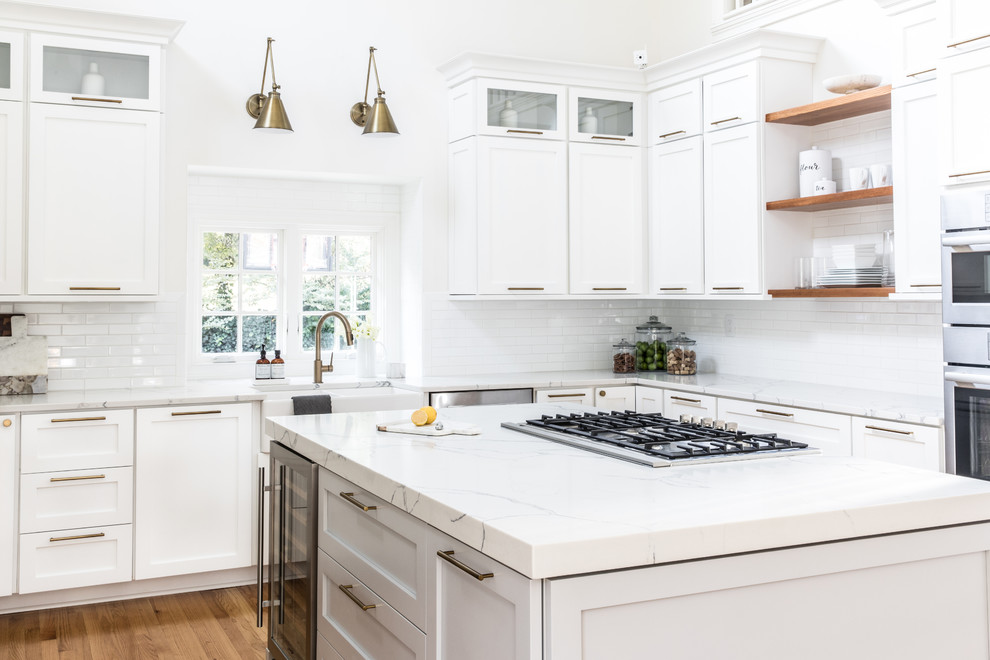 Inspiration for a large transitional u-shaped light wood floor eat-in kitchen remodel in Charlotte with a farmhouse sink, shaker cabinets, white cabinets, quartz countertops, white backsplash, ceramic backsplash, stainless steel appliances and an island