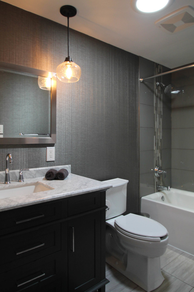 Design ideas for a mid-sized transitional bathroom in Denver with shaker cabinets, grey cabinets, an alcove tub, an alcove shower, a one-piece toilet, gray tile, glass tile, grey walls, porcelain floors, an undermount sink and marble benchtops.