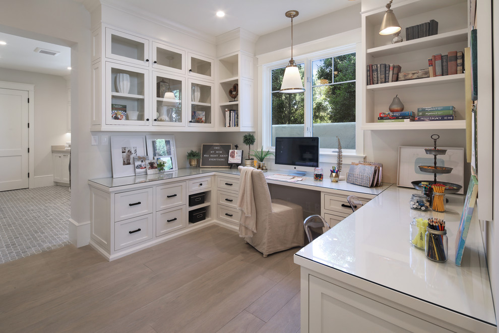 Photo of a transitional home office in Orange County with white walls, medium hardwood floors, a built-in desk and brown floor.