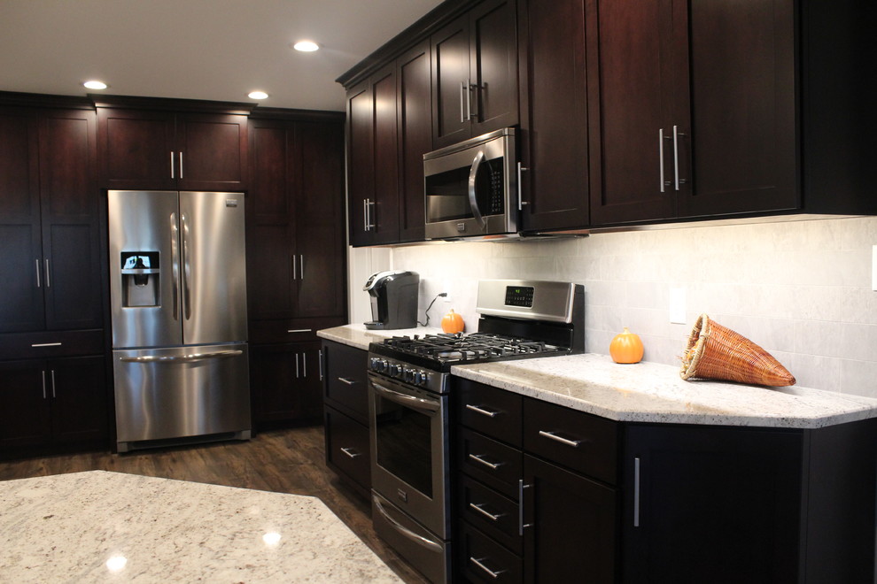Photo of a large traditional l-shaped eat-in kitchen in Philadelphia with a single-bowl sink, shaker cabinets, dark wood cabinets, grey splashback, stainless steel appliances, medium hardwood floors and with island.