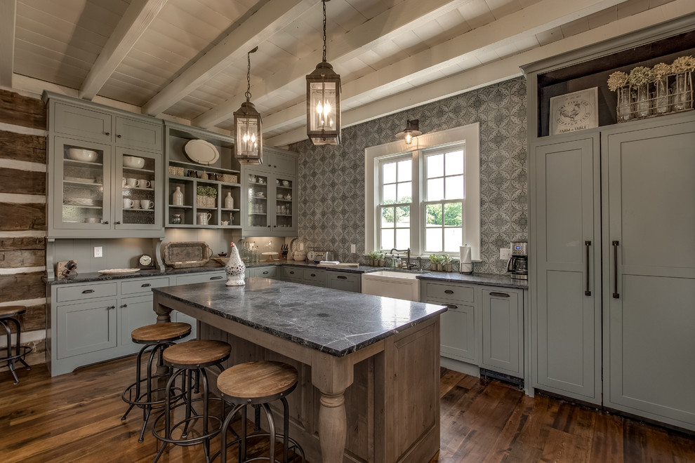 Design ideas for a country l-shaped kitchen in Nashville with a farmhouse sink, grey cabinets, multi-coloured splashback, medium hardwood floors, with island, black benchtop and glass-front cabinets.