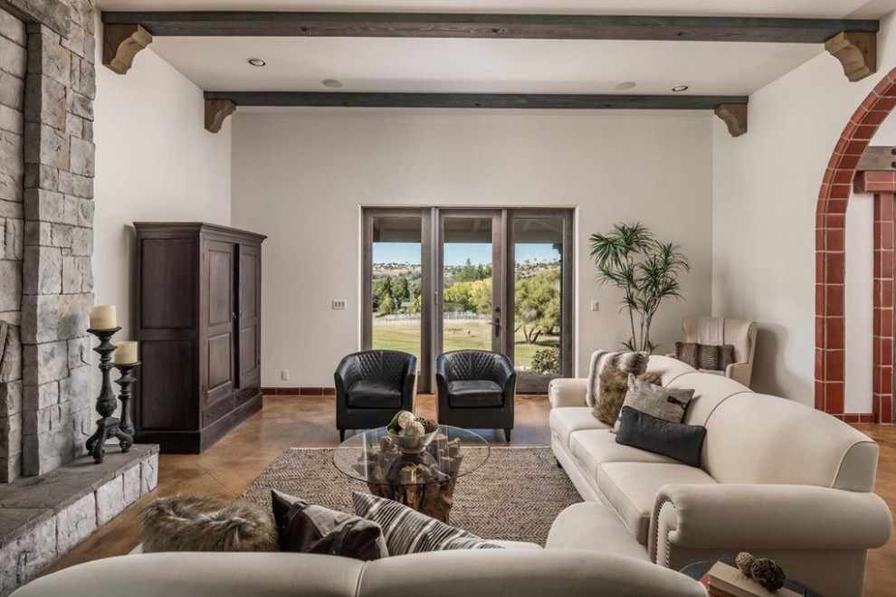 Imagen de sala de estar abierta mediterránea de tamaño medio con paredes blancas, marco de chimenea de piedra, televisor retractable, suelo marrón y vigas vistas
