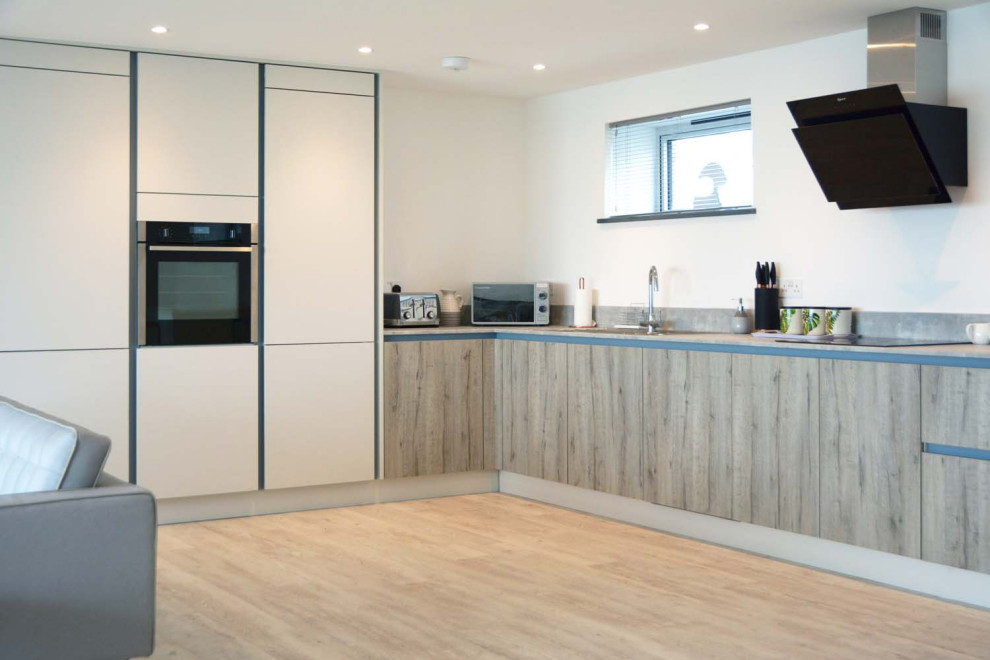 This is an example of a mid-sized scandinavian l-shaped open plan kitchen in Cornwall with flat-panel cabinets, light wood cabinets and laminate benchtops.