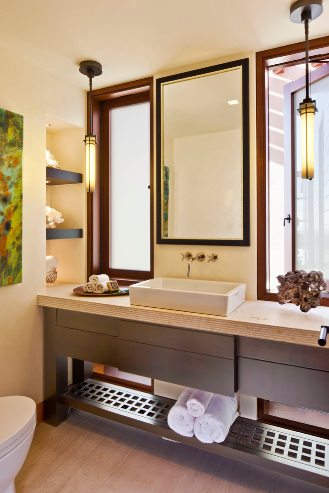 Photo of a contemporary powder room in Los Angeles with a vessel sink, dark wood cabinets, limestone benchtops, beige tile, beige walls, limestone floors and flat-panel cabinets.