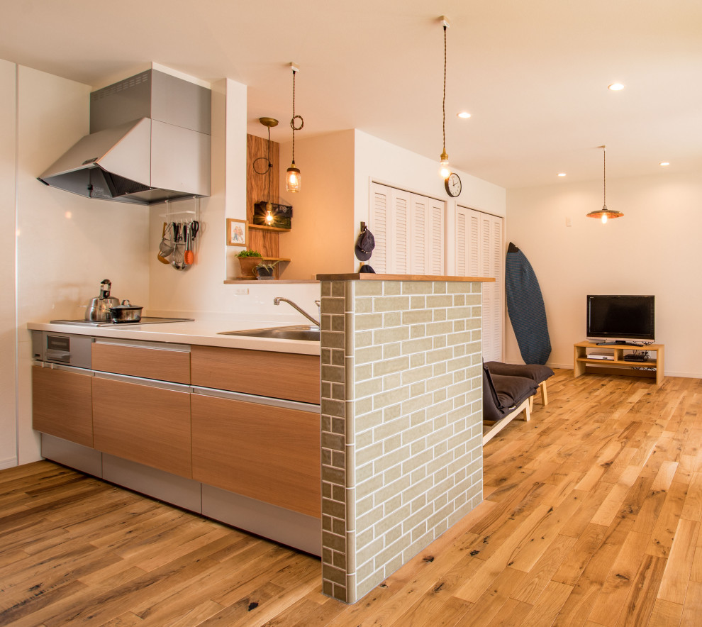 Beach style single-wall open plan kitchen in Other with a single-bowl sink, flat-panel cabinets, medium wood cabinets, solid surface benchtops, white splashback, stainless steel appliances, medium hardwood floors, a peninsula, brown floor, white benchtop and wallpaper.
