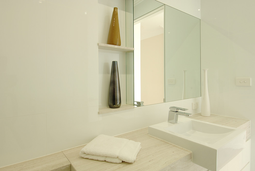 На фото: главная ванная комната среднего размера в стиле модернизм с плоскими фасадами, белыми фасадами, накладной ванной, душем в нише, унитазом-моноблоком, белой плиткой, керамической плиткой, белыми стенами, полом из известняка, настольной раковиной, столешницей из известняка, бежевым полом, открытым душем, бежевой столешницей, нишей, тумбой под одну раковину, подвесной тумбой, многоуровневым потолком и панелями на стенах