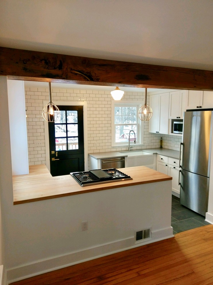 Photo of a small eclectic u-shaped eat-in kitchen in Portland with a farmhouse sink, shaker cabinets, white cabinets, wood benchtops, white splashback, subway tile splashback, stainless steel appliances, slate floors, a peninsula and green floor.