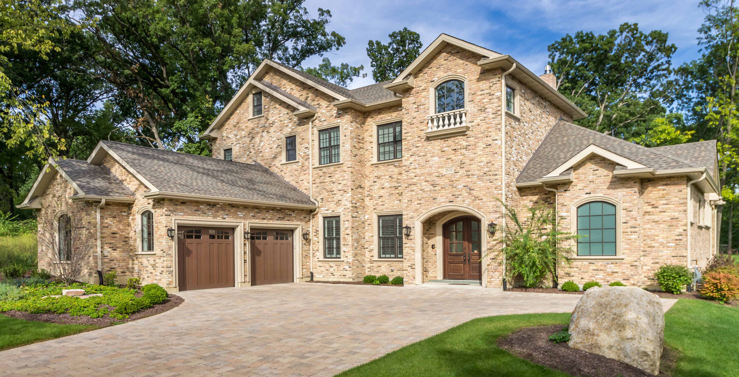 12/12-Architects-designed Elegant brick estate with arched entry, paver driveway, wood garage doors, and mature treescape.