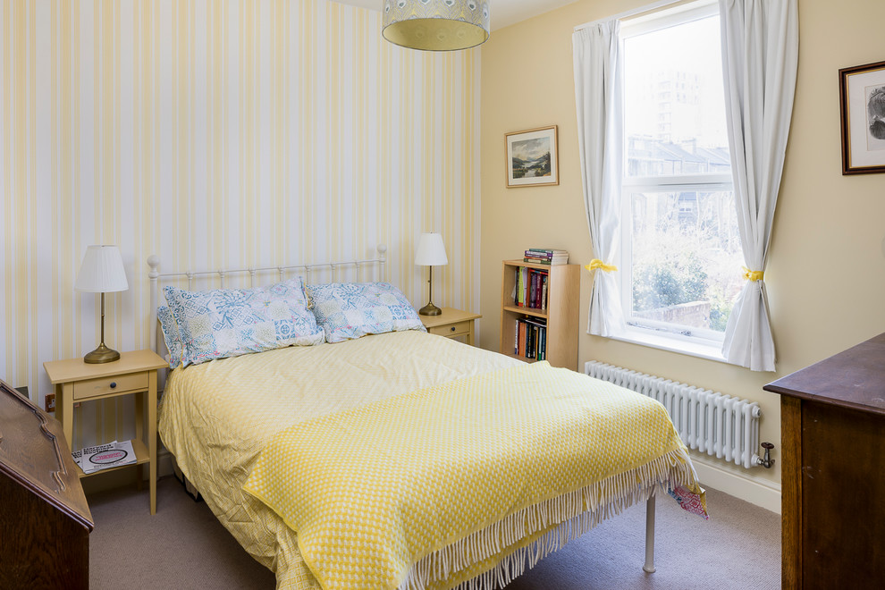 This is an example of a mid-sized transitional guest bedroom in London with yellow walls, carpet and beige floor.
