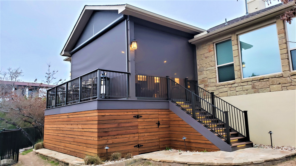 This is an example of a large country backyard and first floor deck in Austin with a roof extension and metal railing.