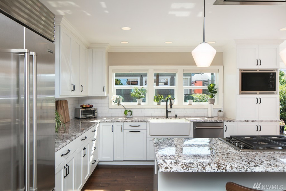 Mid-sized transitional l-shaped medium tone wood floor and brown floor eat-in kitchen photo in Seattle with a farmhouse sink, shaker cabinets, white cabinets, quartz countertops, white backsplash, ceramic backsplash, stainless steel appliances, an island and beige countertops