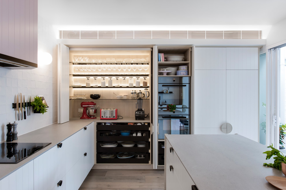 Photo of a mid-sized contemporary l-shaped open plan kitchen in Sydney with a double-bowl sink, white cabinets, recycled glass benchtops, white splashback, cement tile splashback, black appliances, medium hardwood floors, with island and grey benchtop.
