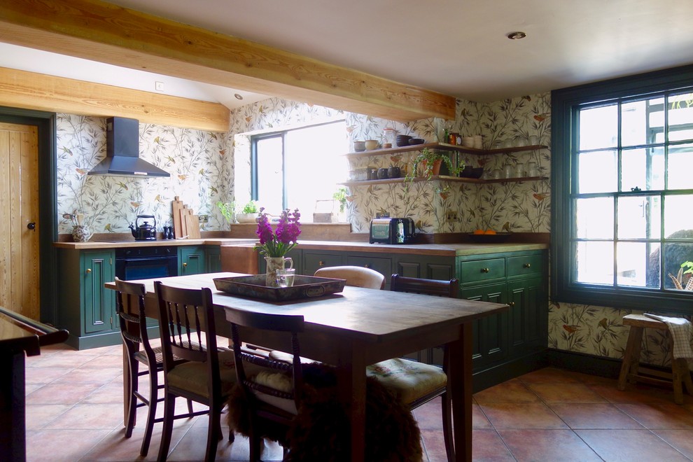 Inspiration for a mid-sized traditional l-shaped eat-in kitchen in Other with a farmhouse sink, shaker cabinets, green cabinets, wood benchtops, glass sheet splashback, black appliances, terra-cotta floors, no island and brown benchtop.