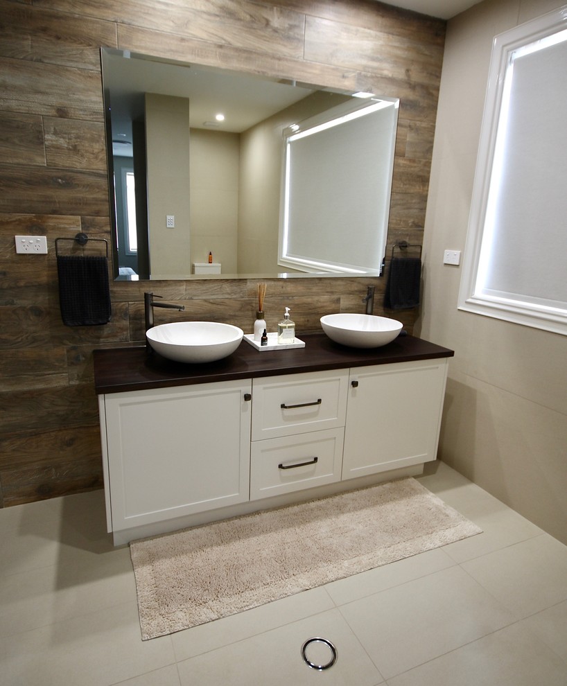 Mid-sized traditional powder room in Sydney with shaker cabinets, white cabinets, a two-piece toilet, beige tile, ceramic tile, multi-coloured walls, ceramic floors, a vessel sink, wood benchtops, beige floor and brown benchtops.