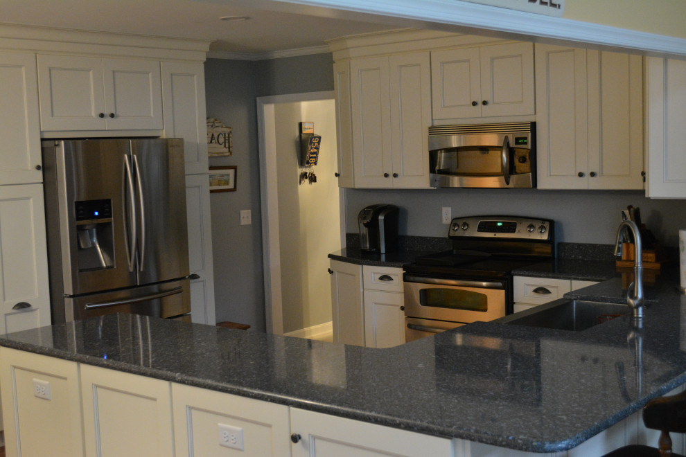 Inspiration for a mid-sized transitional u-shaped dark wood floor and brown floor eat-in kitchen remodel with a farmhouse sink, shaker cabinets, beige cabinets, granite countertops, gray backsplash, mosaic tile backsplash, stainless steel appliances, a peninsula and black countertops