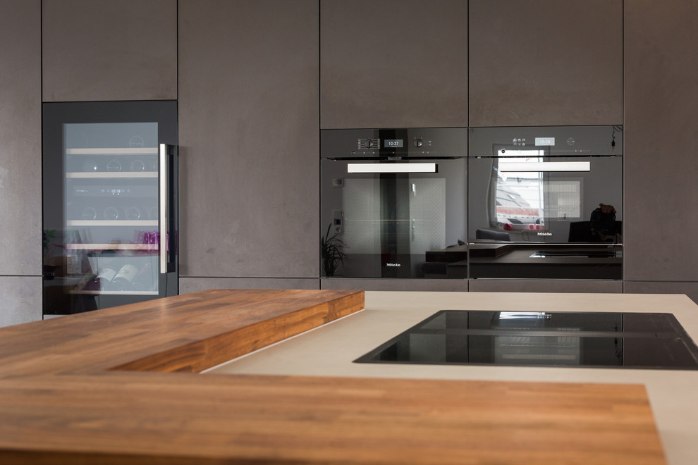 This is an example of a large contemporary l-shaped open plan kitchen in Frankfurt with an integrated sink, flat-panel cabinets, white cabinets, solid surface benchtops, window splashback, black appliances, with island, grey floor and grey benchtop.