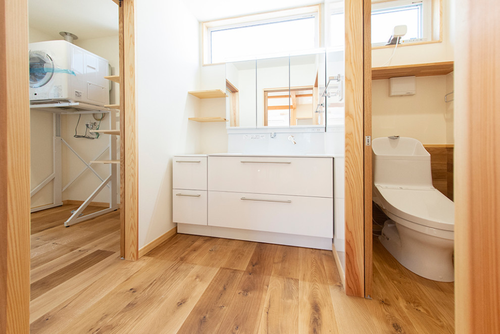 Cette photo montre un grand WC et toilettes scandinave avec des portes de placard blanches, un mur blanc, un sol en bois brun, un sol beige et un plan de toilette blanc.