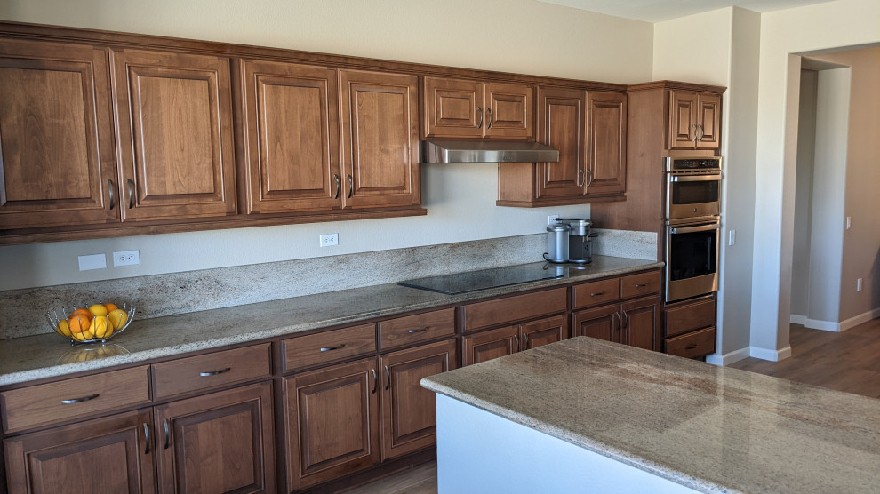 Mid-sized transitional l-shaped open plan kitchen in Phoenix with a drop-in sink, raised-panel cabinets, medium wood cabinets, granite benchtops, beige splashback, granite splashback, stainless steel appliances, porcelain floors, with island, beige floor and beige benchtop.