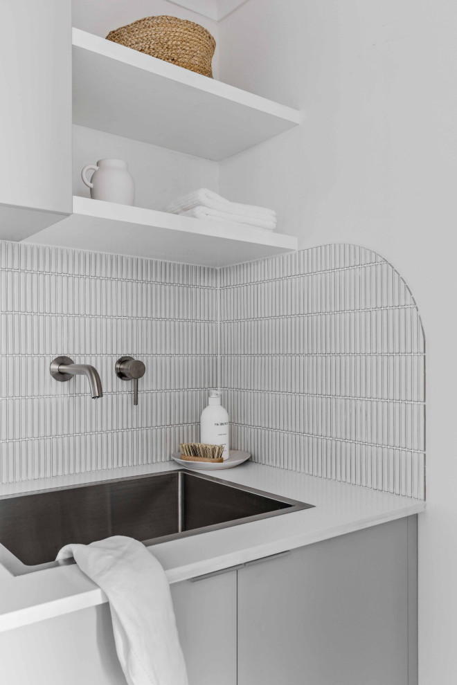 Exempel på en liten modern vita linjär vitt tvättstuga enbart för tvätt, med en nedsänkt diskho, släta luckor, grå skåp, bänkskiva i kvarts, vitt stänkskydd, stänkskydd i mosaik, vita väggar, klinkergolv i porslin, en tvättpelare och grått golv