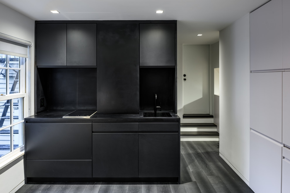 Design ideas for a small modern single-wall eat-in kitchen in New York with an integrated sink, flat-panel cabinets, black cabinets, solid surface benchtops, black splashback, panelled appliances, dark hardwood floors and no island.