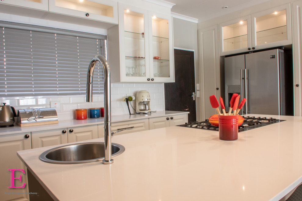 Example of a mid-sized classic l-shaped eat-in kitchen design in Other with raised-panel cabinets, white cabinets, quartz countertops, white backsplash, subway tile backsplash, stainless steel appliances, an island and white countertops