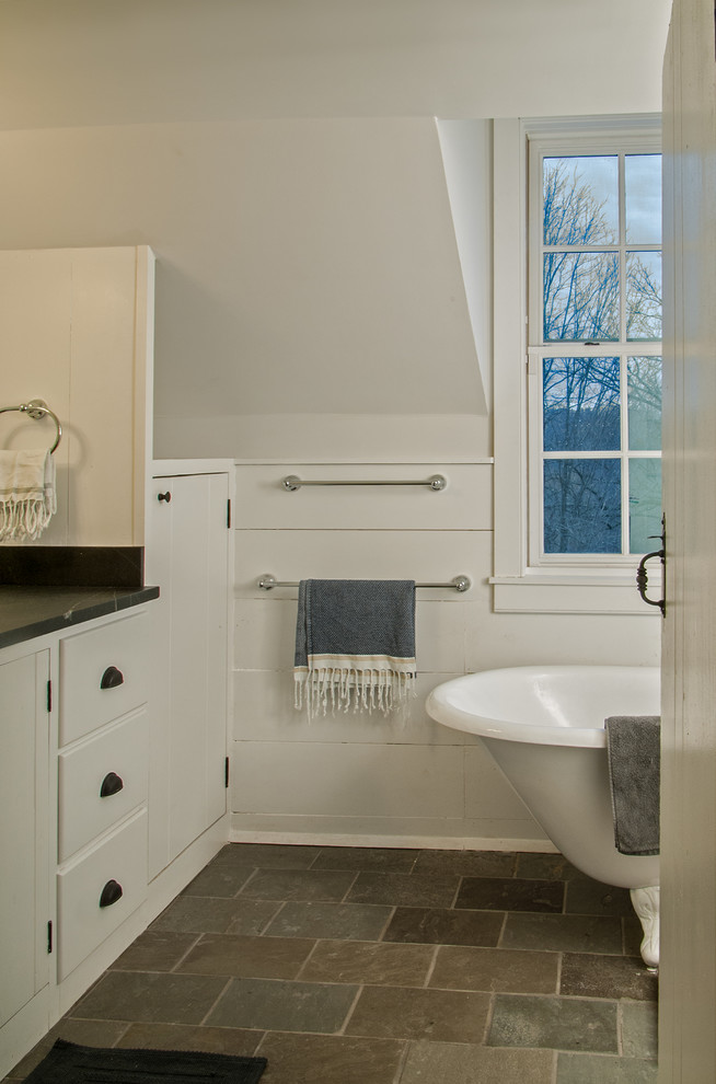 This is an example of a mid-sized country 3/4 bathroom in New York with white cabinets, soapstone benchtops, a claw-foot tub, stone tile, white walls and slate floors.