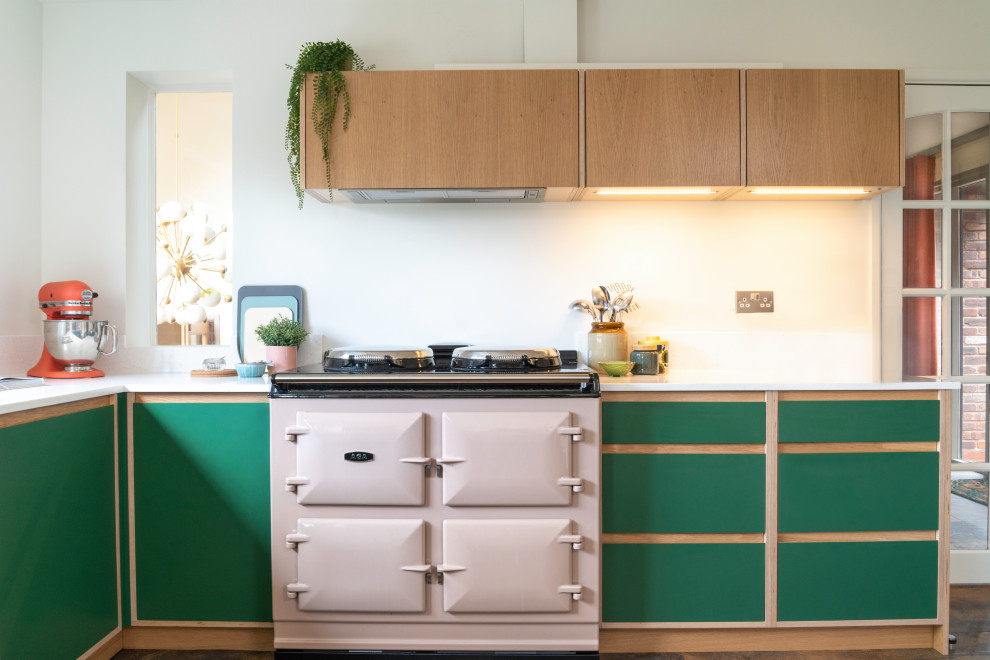 Photo of a mid-sized midcentury u-shaped eat-in kitchen in West Midlands with an integrated sink, flat-panel cabinets, green cabinets, solid surface benchtops, white splashback, glass tile splashback, coloured appliances, vinyl floors, with island, multi-coloured floor and white benchtop.