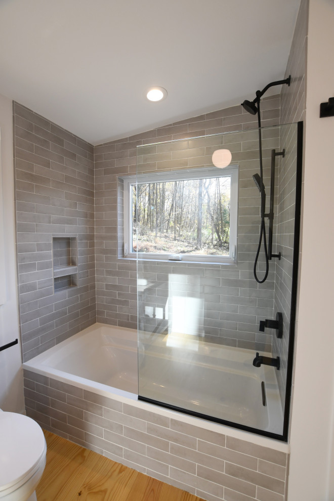Design ideas for a mid-sized midcentury master bathroom in New York with open cabinets, black cabinets, a drop-in tub, a shower/bathtub combo, a two-piece toilet, gray tile, subway tile, white walls, light hardwood floors, a vessel sink, engineered quartz benchtops, an open shower and grey benchtops.