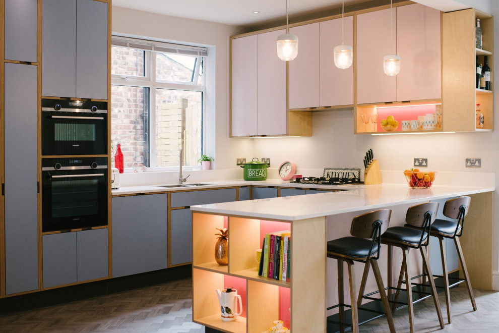 Scandinavian u-shaped kitchen in Manchester with a double-bowl sink, flat-panel cabinets, blue cabinets, black appliances, a peninsula, brown floor and white benchtop.
