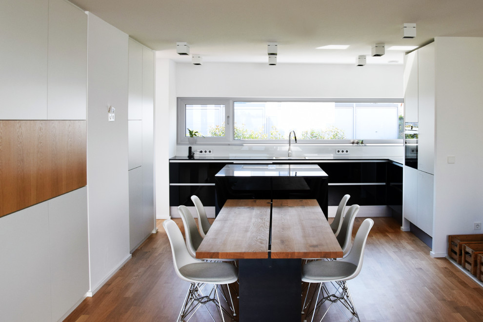 Photo of a mid-sized contemporary l-shaped open plan kitchen in Frankfurt with flat-panel cabinets, black cabinets, black appliances, medium hardwood floors and with island.
