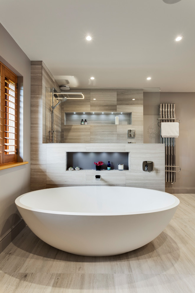 This is an example of a large contemporary master bathroom in Sussex with flat-panel cabinets, light wood cabinets, a freestanding tub, an open shower, a two-piece toilet, gray tile, stone slab, grey walls, limestone floors, a drop-in sink and marble benchtops.