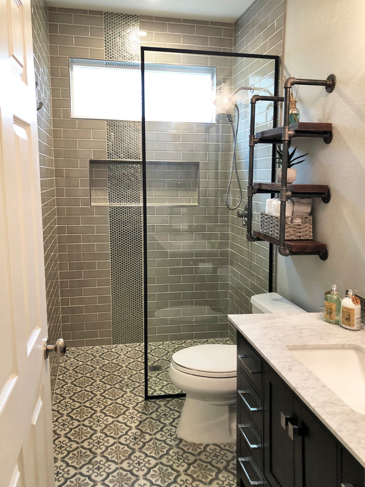 Photo of a small industrial bathroom in Dallas with shaker cabinets, black cabinets, a curbless shower, a one-piece toilet, brown tile, subway tile, grey walls, porcelain floors, an undermount sink, marble benchtops, multi-coloured floor, an open shower and white benchtops.
