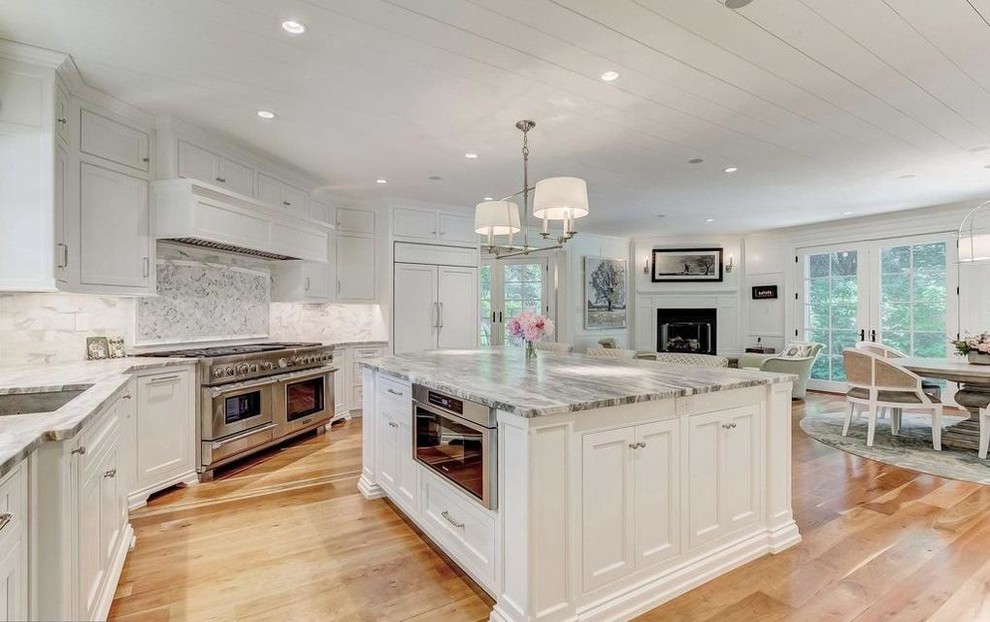 Open concept kitchen - large transitional u-shaped light wood floor and beige floor open concept kitchen idea in Baltimore with an undermount sink, recessed-panel cabinets, white cabinets, marble countertops, gray backsplash, marble backsplash, paneled appliances, an island and gray countertops