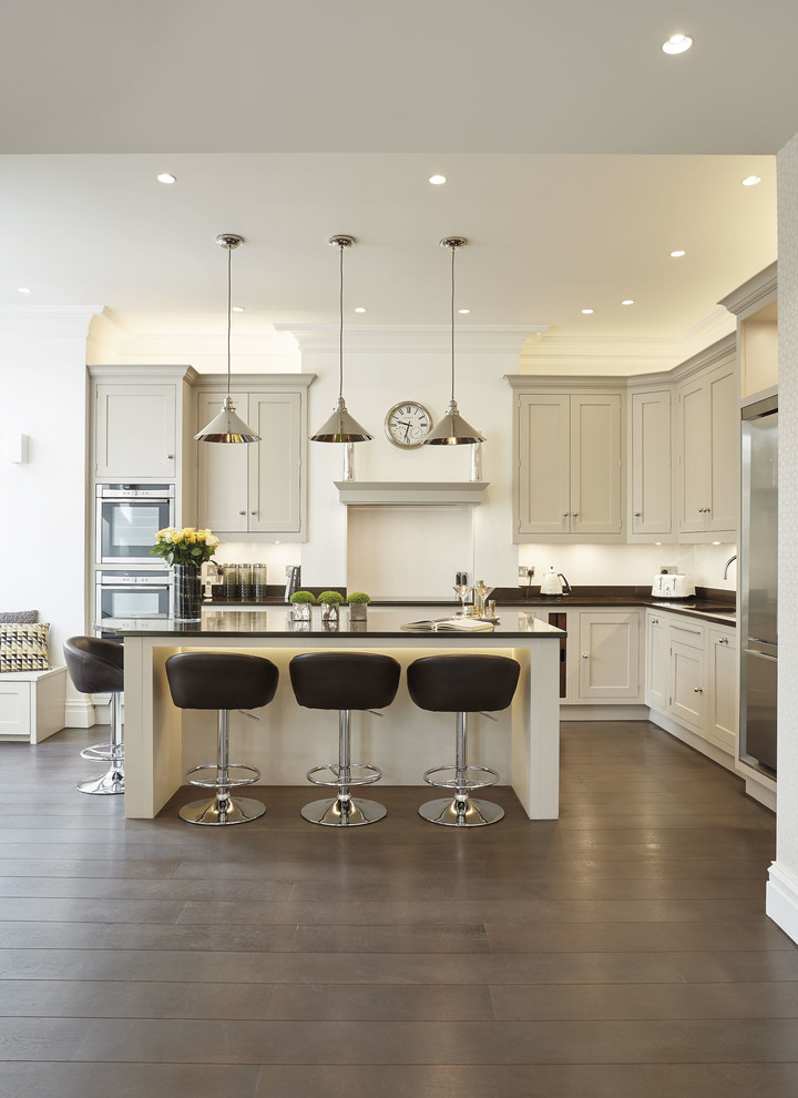 This is an example of a large contemporary l-shaped eat-in kitchen in London with an integrated sink, shaker cabinets, grey cabinets, quartzite benchtops, black splashback, stainless steel appliances, with island and black benchtop.