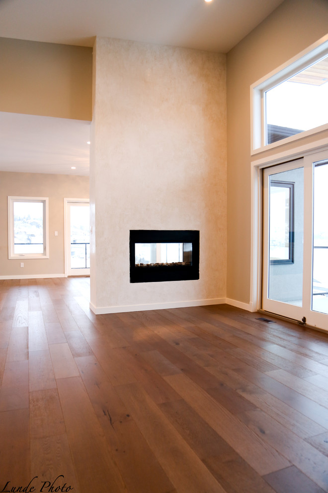 This is an example of a large modern formal open concept living room in Vancouver with grey walls, light hardwood floors, a two-sided fireplace, a plaster fireplace surround and no tv.