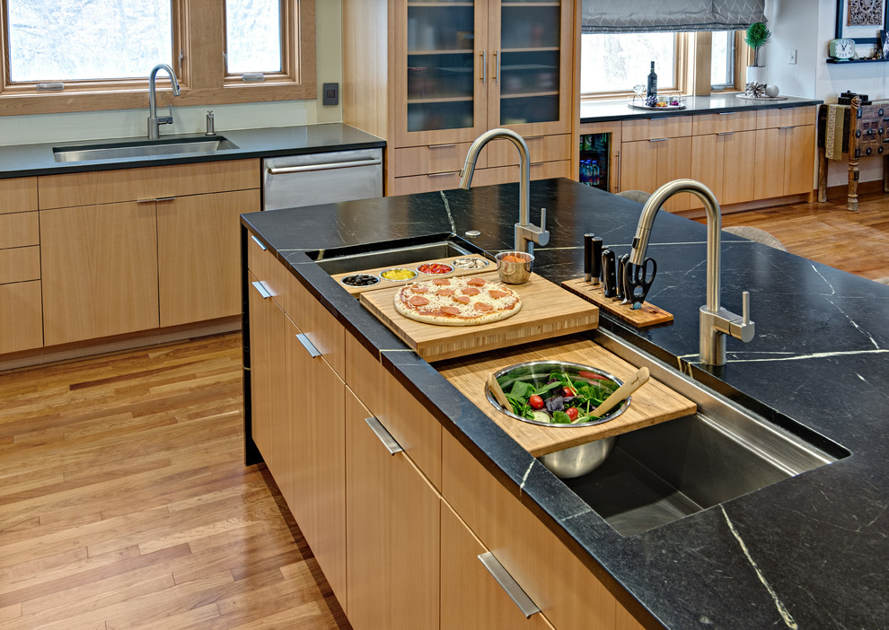 Design ideas for a mid-sized contemporary l-shaped eat-in kitchen in Minneapolis with an undermount sink, flat-panel cabinets, medium wood cabinets, soapstone benchtops, green splashback, glass sheet splashback, stainless steel appliances, medium hardwood floors, with island, orange floor and green benchtop.