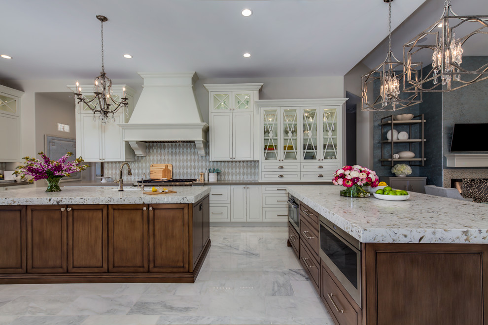 Inspiration for a large transitional l-shaped eat-in kitchen in Phoenix with a drop-in sink, glass-front cabinets, white cabinets, granite benchtops, beige splashback, ceramic splashback, stainless steel appliances, marble floors, multiple islands and white floor.
