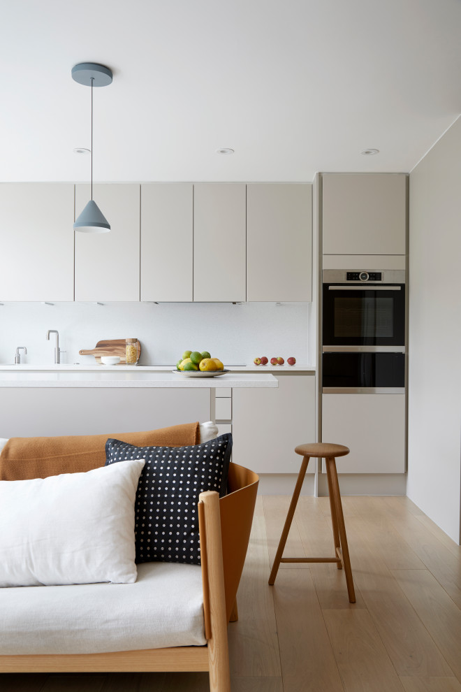 Design ideas for a small contemporary single-wall open plan kitchen in London with an integrated sink, flat-panel cabinets, white cabinets, solid surface benchtops, white splashback, engineered quartz splashback, stainless steel appliances, medium hardwood floors, no island, yellow floor, white benchtop and wallpaper.