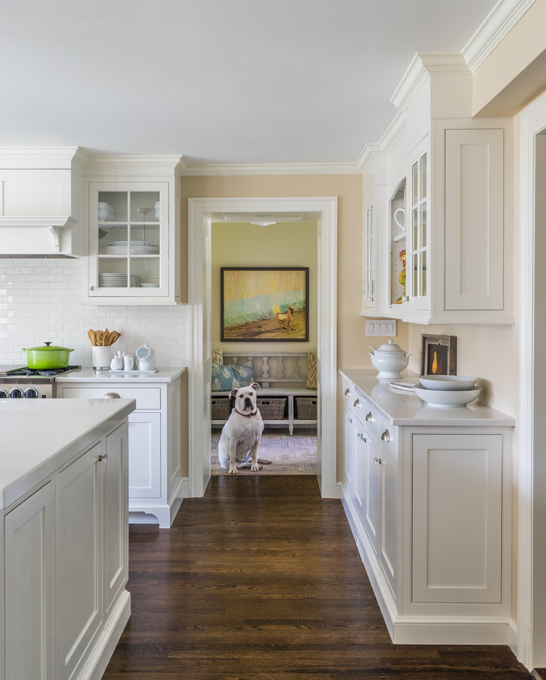 Inspiration for a large country l-shaped eat-in kitchen in Boston with a farmhouse sink, recessed-panel cabinets, white cabinets, quartz benchtops, white splashback, ceramic splashback, stainless steel appliances, medium hardwood floors, with island and brown floor.