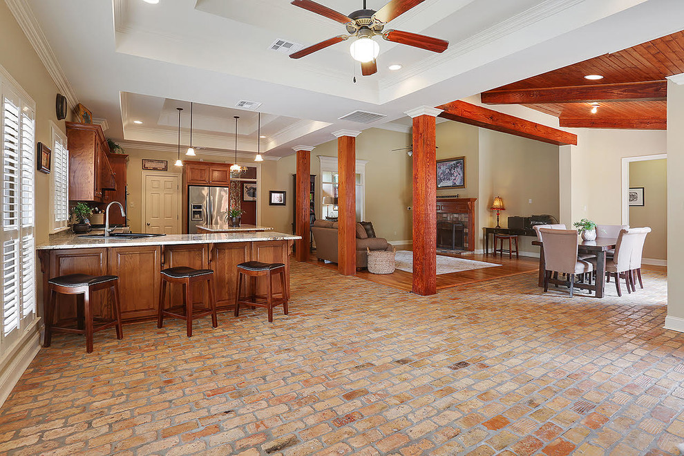 Photo of a mid-sized traditional l-shaped open plan kitchen in New Orleans with raised-panel cabinets, medium wood cabinets, granite benchtops, beige splashback, subway tile splashback, stainless steel appliances, brick floors and with island.