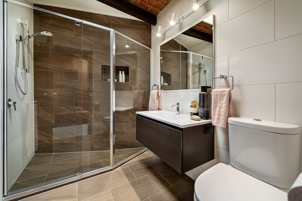 Photo of a small midcentury master bathroom in Melbourne with flat-panel cabinets, dark wood cabinets, a corner shower, a two-piece toilet, brown tile, porcelain tile, white walls, porcelain floors, an integrated sink, brown floor, a hinged shower door and white benchtops.