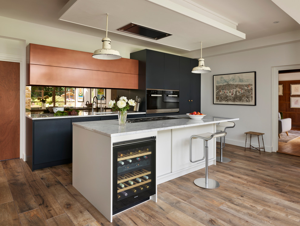 Photo of a large modern l-shaped eat-in kitchen in London with an integrated sink, blue cabinets, marble benchtops, metallic splashback, mirror splashback, light hardwood floors, with island, brown floor, white benchtop, flat-panel cabinets and stainless steel appliances.